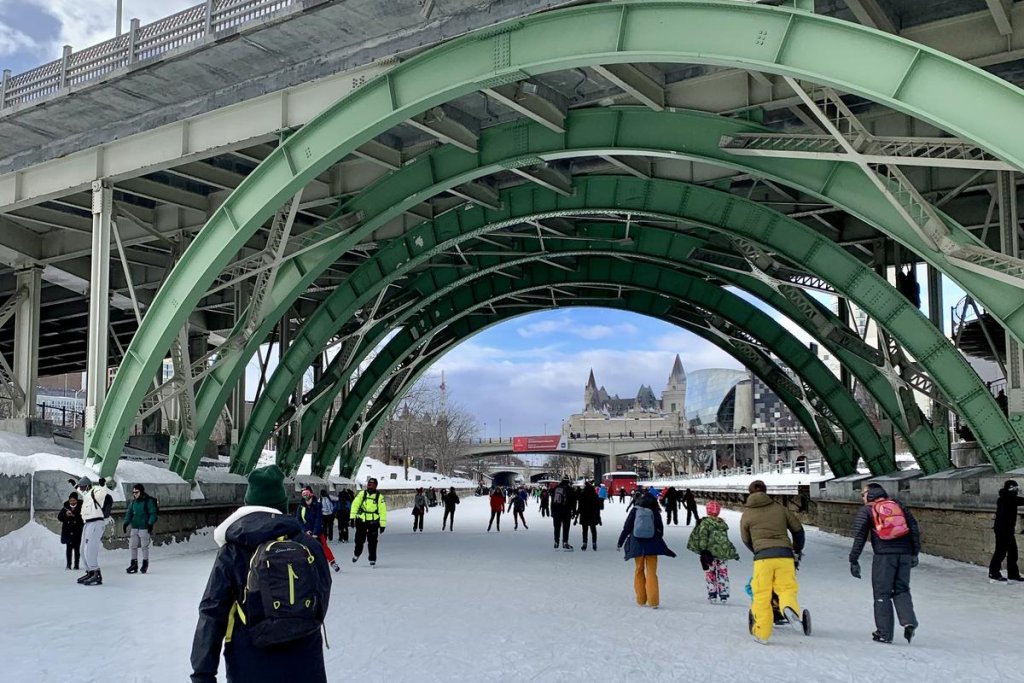 Patineurs sur la patinoire du canal Rideau à Ottawa, sous les arches du pont Mackenzie King, avec le Château Laurier au loin