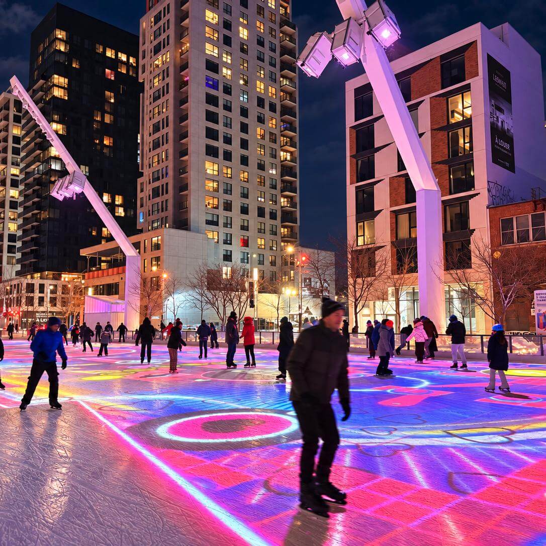 Patineurs sur la glace illuminée de projections colorées à la patinoire de l’Esplanade Tranquille, à Montréal